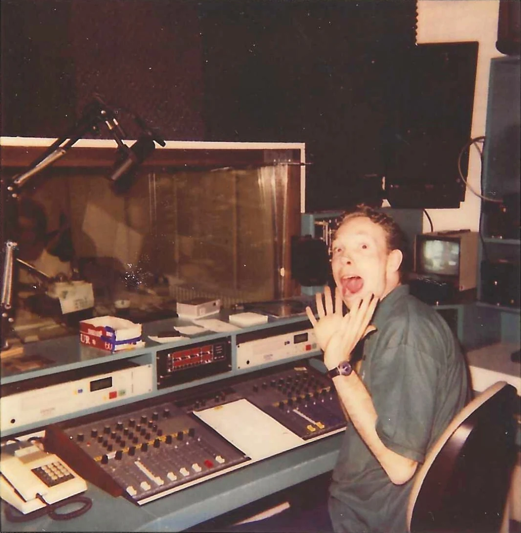 Richard at the mixing desk of a radio station, gesturing towards the camera